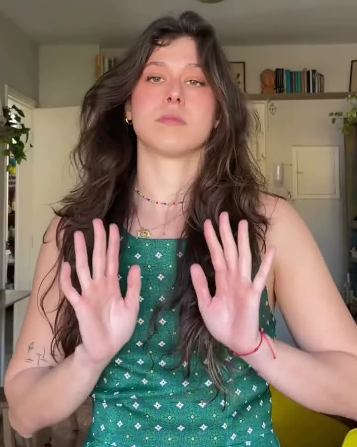 Mica de vestido verde na cozinha, falando com as mãos abertas